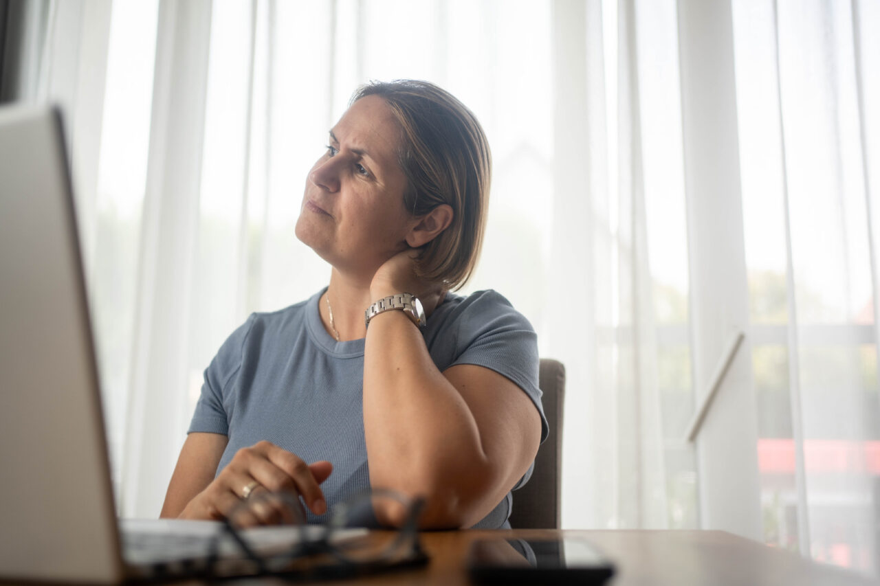Woman at desk with hand on neck