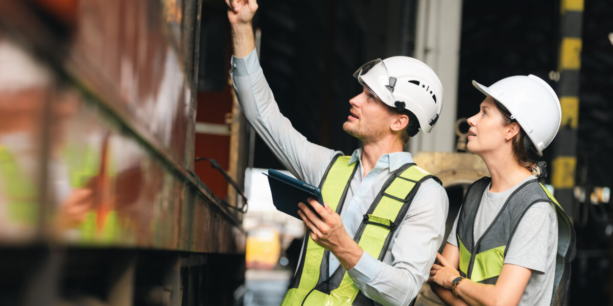 Engineers wearing safety helmets inspecting railway blueprint beside a vintage locomotive, symbolizing teamwork, innovation, and development in modern rail transportation and infrastructure projects