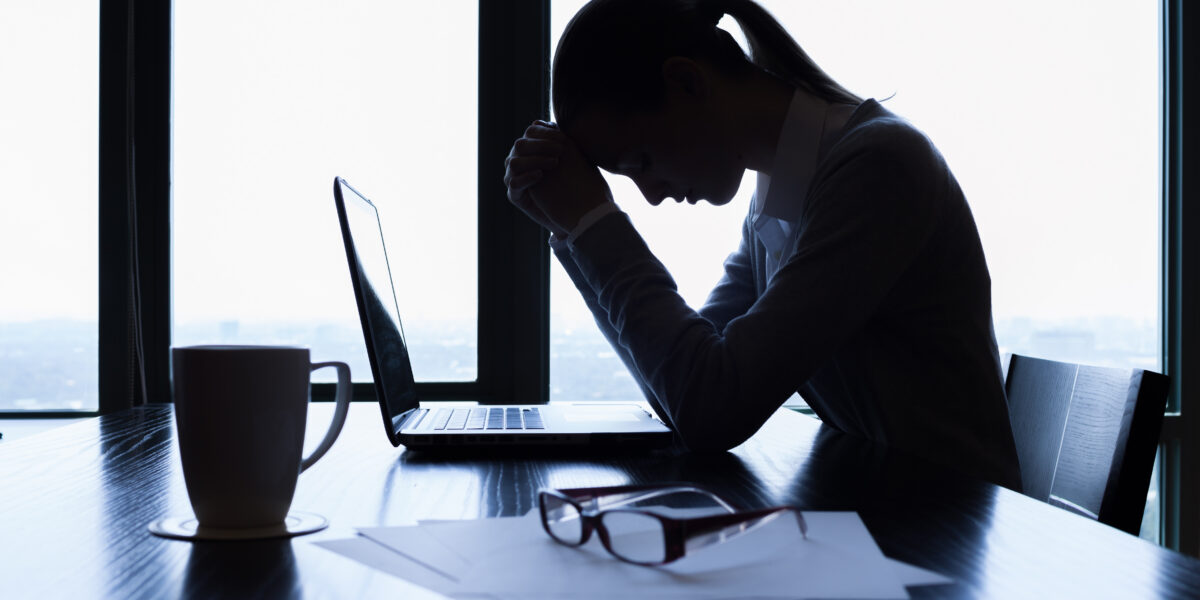 Individual at desk with laptop, reviewing documents and seeking legal advice; office lit by daylight through large windows.
