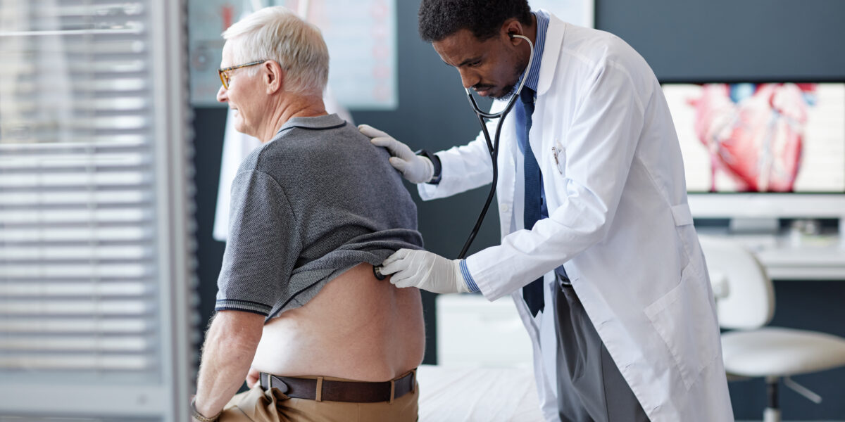 Doctor examines older male patient's back, assessing injuries related to Queensland work injury damages claims in clinic setting.