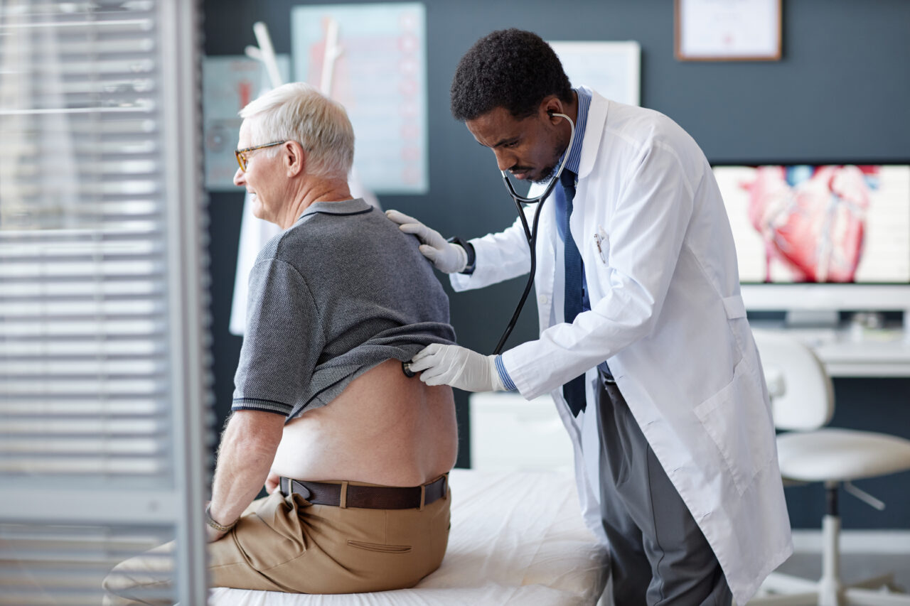 Doctor examines older male patient's back, assessing injuries related to Queensland work injury damages claims in clinic setting.