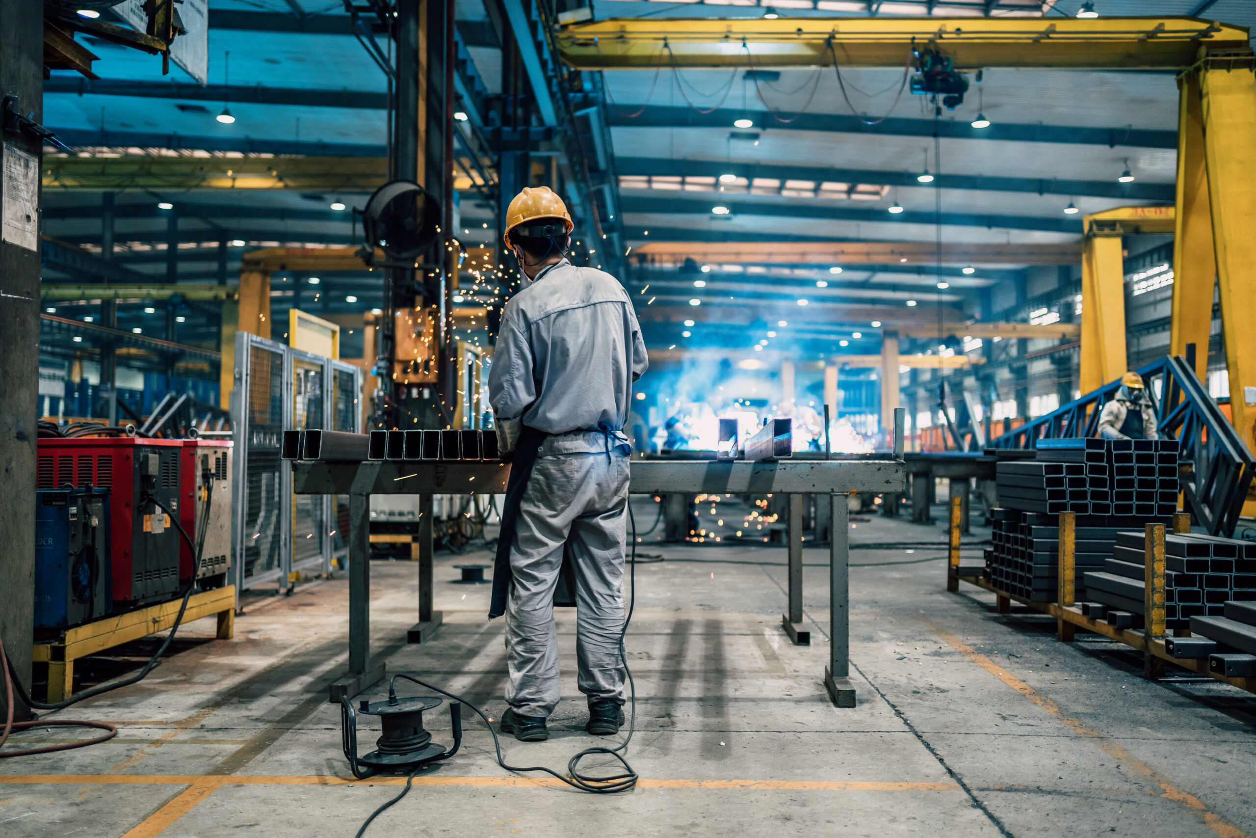 Industrial worker in protective gear at factory workstation; sparks highlight the importance of workplace safety and legal protection.